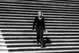 Marjorie Taylor Greene in a pantsuit walking down stone steps toward the camera. Black-and-white.