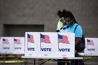 A photo of a black woman wearing a face mask voting at a poll booth in Kentucky.