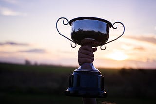 Child holding up a trophy against a sunset.