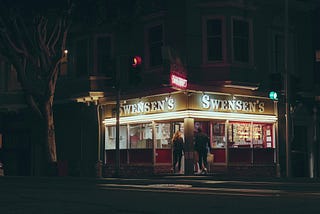 The exterior of Swensen’s at night, its signs lit up.