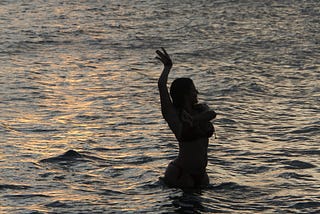 Women silhouetted in water in flamenco pose at sundown.