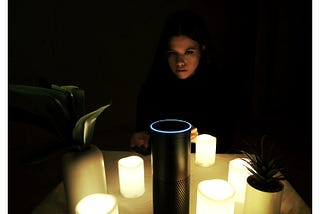 The author sits in the dark behind the Amazon Echo, which is surrounded by lit candles in a seance-style set up.