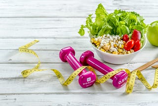 Two .5 kg dumbbells, measuring tape, and a salad on a rustic wooden table.