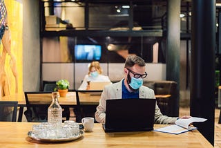Businesspeople wearing masks in the office and sitting at further distances.