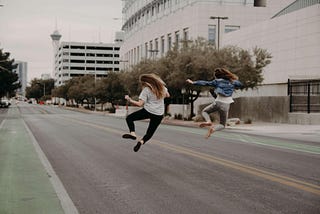 two girls jumping in the air in the middle of city road, they look like they succeeded