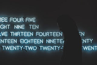 Silhouette of a person walking in front of a wall of numbers spelled out in glowing blue neon.