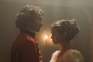 A couple dressed in royal attire standing facing each other in a candlelit room