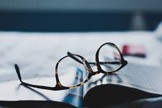 pair of dark-framed eyeglasses placed upside down on a magazine or book.