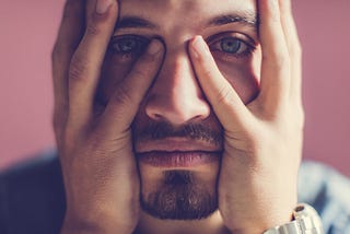 A photo of a man with a serious expression holding his face with his two hands.