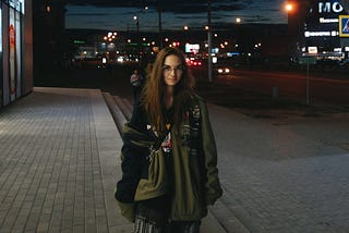 A woman is standing on a city sidewalk at night.