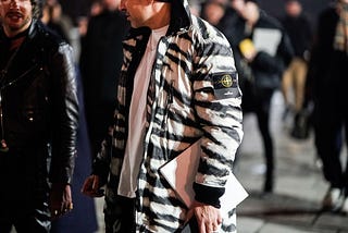 A man wears a black and white zebra print bomber jacket from the brand “Stone Island.”