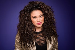 Portrait photo of Michelle Buteau in front of an indigo background.