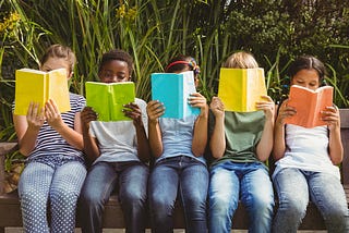 Children reading books at a park.