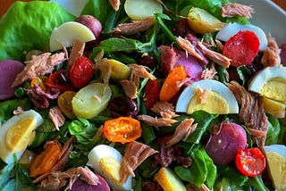 A plate piled high with a vibrant salad containing ingredients like sliced boiled eggs, cherry tomatoes, and shreds of meat.