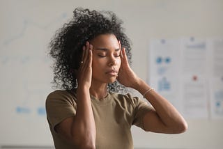 A photo of an exhausted black women with her hands on her temples.