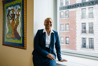Rev. Dr. LaKeesha Walrond laughs while sitting on a window ledge in her fifth floor Upper Manhattan office.