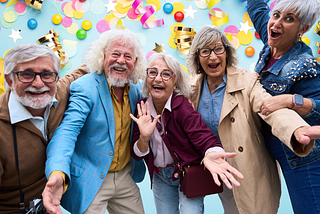 A joyful group of vibrant, stylish older adults smiling, laughing, and celebrating together against a bright blue background filled with colorful confetti and gold streamers.