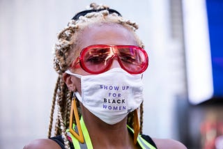 Black woman wearing a face mask that says “Show up for Black women.”