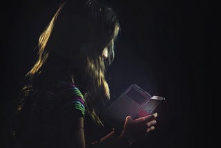 Dark photo of a young girl on a smartphone.