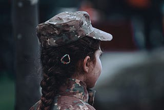 A short woman in fatigues faces away from the camera