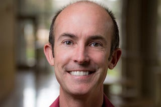 Head shot of Professor Ryan Hibbs smiling with background blurred.