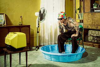 A man finds relief from the heat of summer with a swim cap and a kiddie pool in his living room