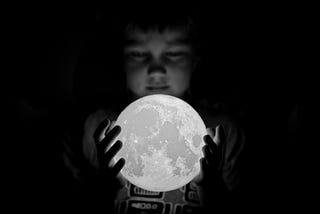 Black and white photo of a young boy holding a moon figure in his hands.