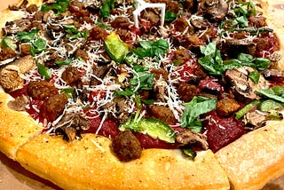 A photo of a pizza hut pizza taken from one side, no regular cheese but deep red sauce, vegan sausage, veggies, & parmesan