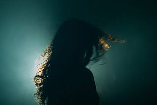 A dark photo of a rear view of a woman turning her head.