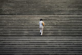 A solitary woman with her back to the camera climbing full-width stairs.