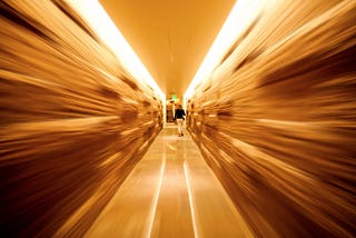 A blurred image of an aisle in a grocery store, focused on the center where a woman is walking.