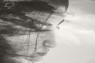 A black and white superimposed photo of a cloudy sky and a woman’s face.