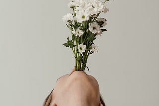 A person with their head leaned all the way back holding a bunch of long-stemmed flowers in their mouth like a vase.