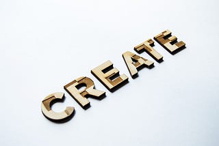 The word ‘create’ is spelt out in capitalised wooden letters against an off-white backdrop.
