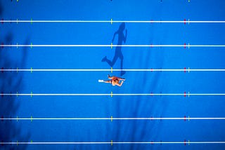 An aerial photo of a person running on a track. Their shadow looks like it’s running.