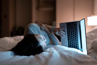 A photo of a woman on her laptop, lying in bed.
