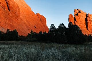 Red Rocks in Colorado Springs juts out of the ground as monoliths above the trees in the forefront.