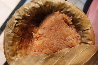 Inside a dried leaf container, a brown colored pudding is served.