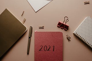 A few journals and stationary. The journal at the center is red and has “2021” inscribed on its cover.