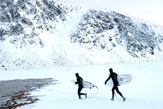 Surfers run across the snow toward Unstad beach in Norway.