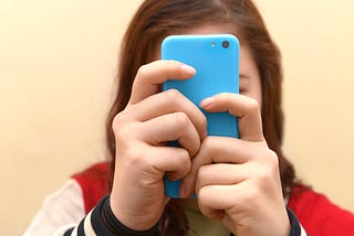 Close up of a teenager using her smartphone. Her face is obscured by her phone.