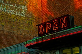 A photo of a neon OPEN sign on top of a business storefront.