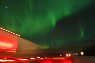 Abstract color photograph of faded, but apparent, green aurora in the sky with red glow from passing traffic in the foreground.
