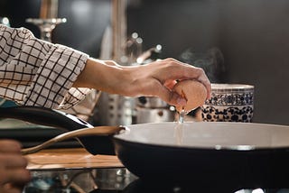 Close up of unrecognizable woman cracking an egg for breakfast while putting it in a frying pan.