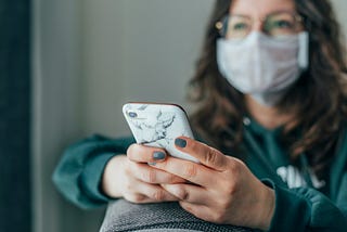 A person wearing a face mask, using their phone. They seem to have an optimistic expression.