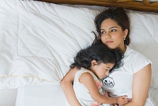 Tired South Asian mother holding her sleeping daughter.