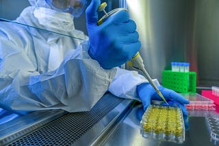 Photo of a researcher wearing gloves and safety gear pipetting into tubes.