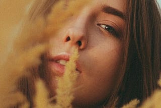 Calm young woman looking at camera through tall reeds in nature.