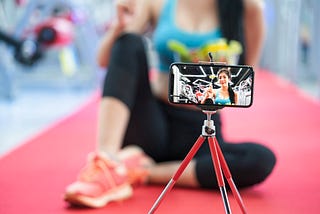 A photo of a woman recording herself doing a workout using her smartphone on a tripod.
