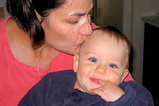 Closeup of a Mom kissing the top of her baby’s head, while baby is smiling at camera.